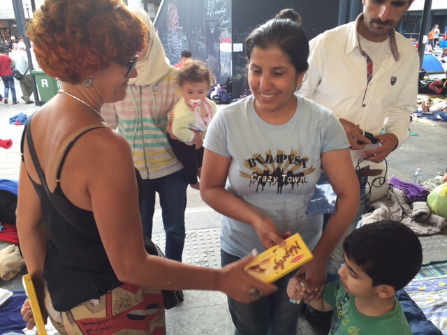 Expressão facial de uma mãe refugiada vendo seu filho receber um pacote de biscoito.